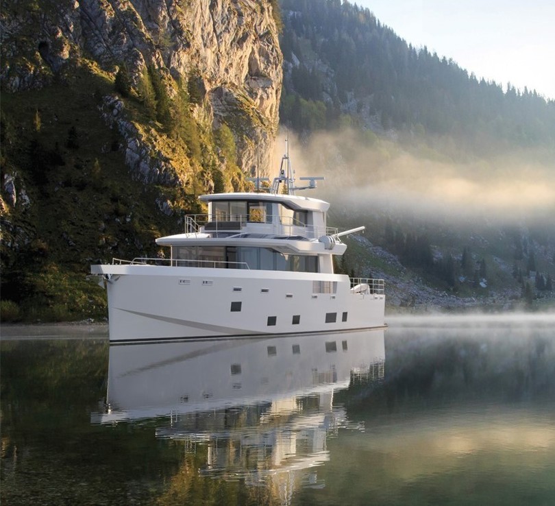 Arksen 85 Explorer Yacht on the water in front of mountains and trees.