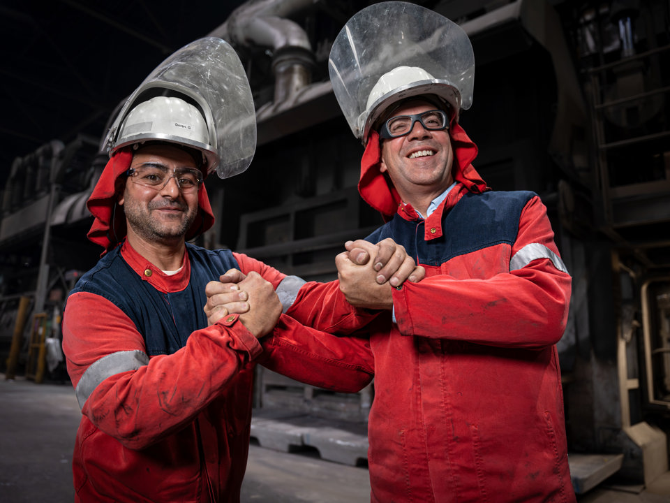 Two Speira employees in work clothes shake hands with a smile in an aluminium plant.