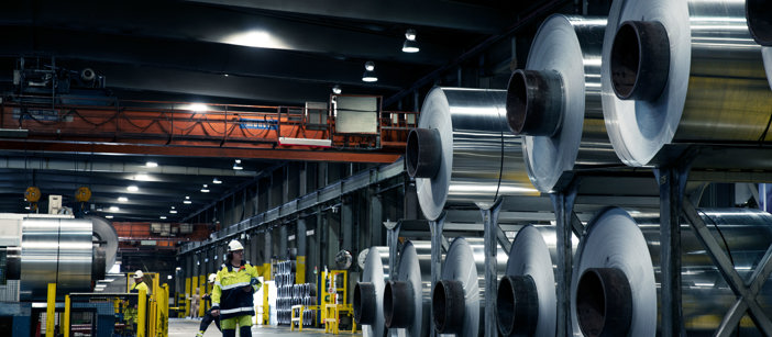 Speira factory worker standing next to stacked up aluminium coils.