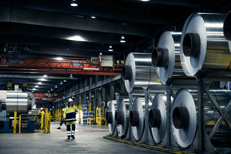 Speira factory worker standing next to stacked up aluminium coils.