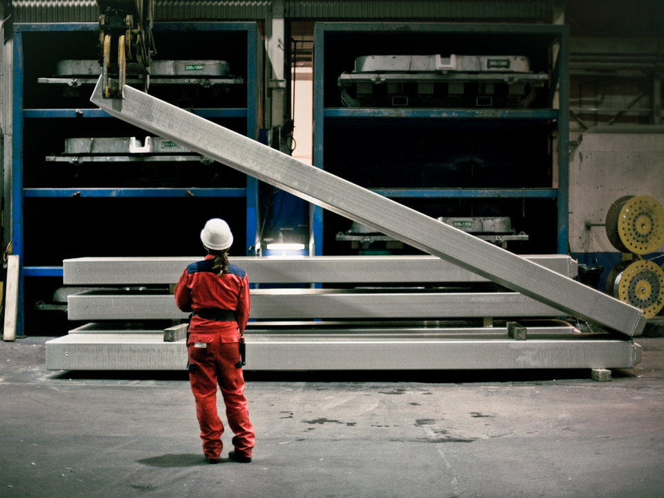 Speira employee in a factory standing in front of aluminium ingoits being lifted.