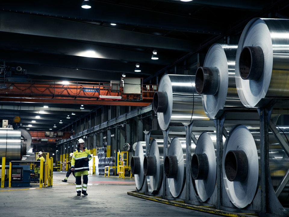 Aluminium coils stacked up in a factory with a Speira employee standing next to them.