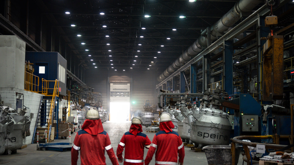 Three Speira employees walk through one of the Speira plants in their work clothes.