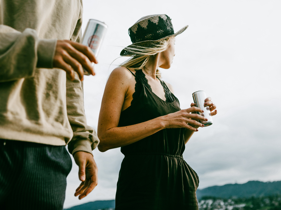 Two people holding beverage cans and looking at the distant landscape.