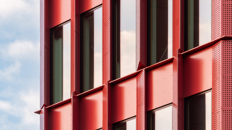 Fenster eines Gebäudes, umgeben von einer roten Aluminiumfassade.