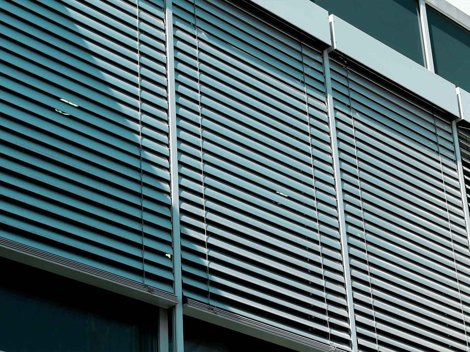 Aluminium raffstores in front of a modern building’s window front.