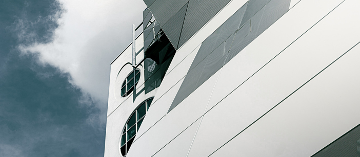 A building’s façade made of aluminium reflecting the blue sky in the back.