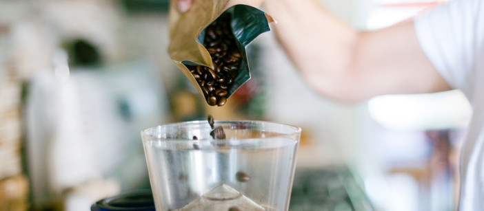 Coffee beans from an aluminium bag being poured into a grinding machine.