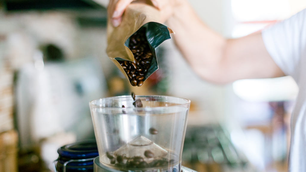 Coffee beans from an aluminium bag being poured into a grinding machine.