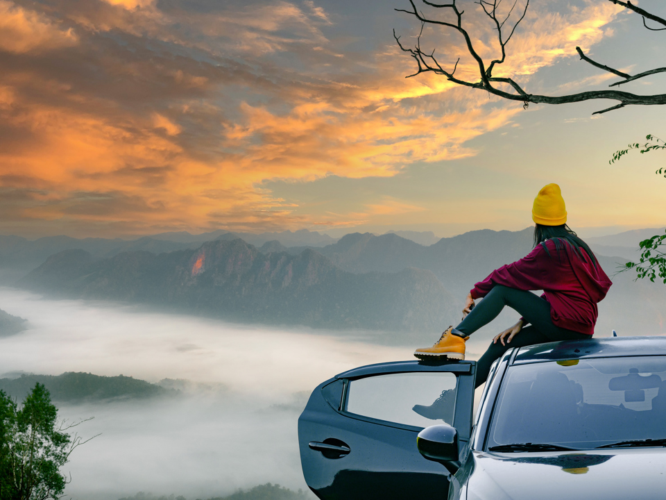 Woman sitting on a car roof in nature with a view of a sunset.