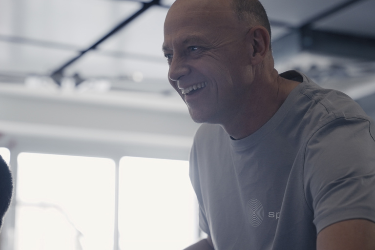 A smiling Speira employee in a work shirt looks at a monitor in the office.