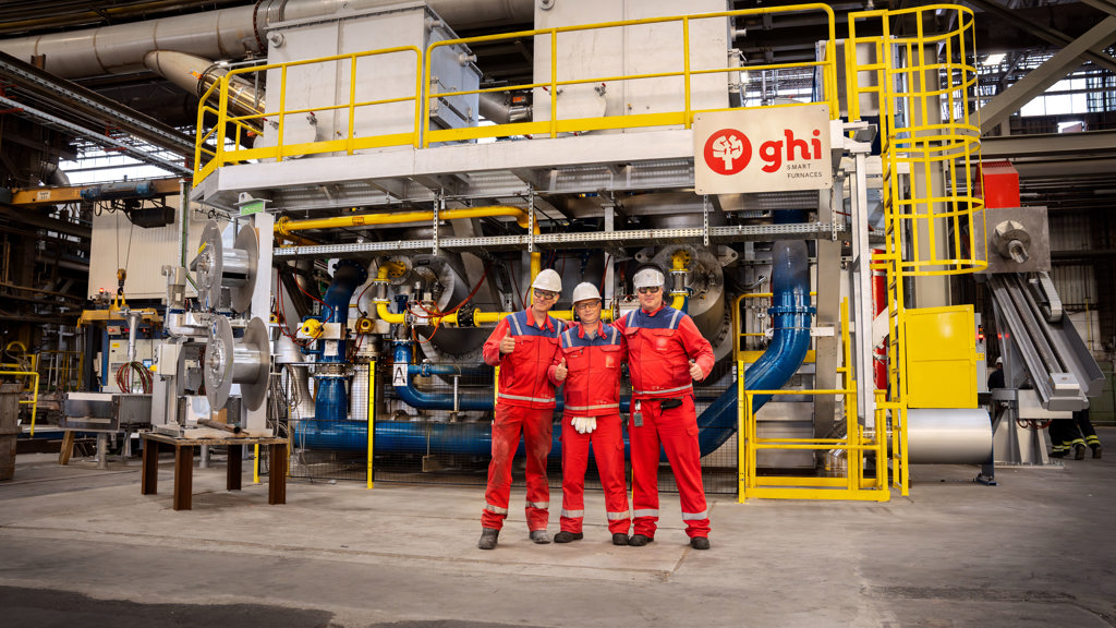 Three Speira employees in workwear stand in front of a new oven in Speira’s plant in Hamburg.