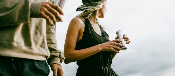 Two people holding beverage cans and looking at the distant landscape.