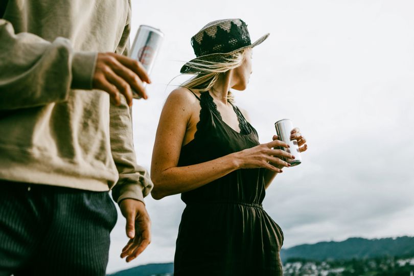 Two people holding beverage cans and looking at the distant landscape.