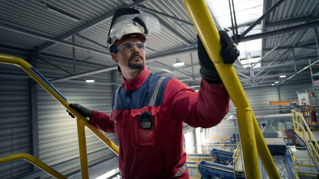 A Speira employee in work clothes holds on to the yellow handrail of a staircase.